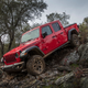 A red Jeep Gladiator pickup driving down a muddy bank
